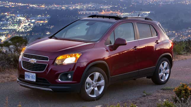 A phot of a burgundy Chevrolet Trax SUV with the lights of a city in the background. 