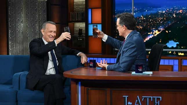 Tom Hanks and Stephen Colbert lifting glasses