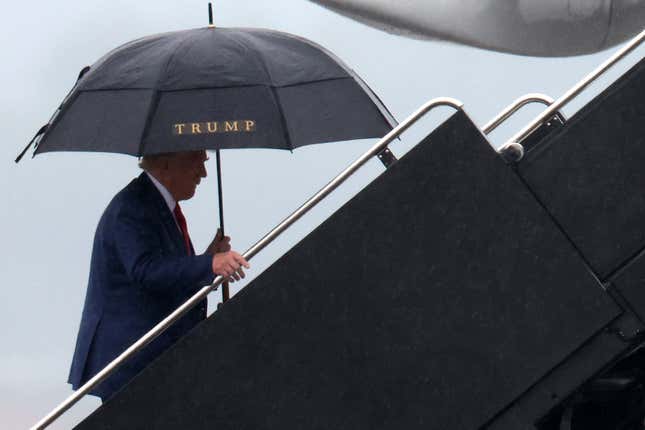 Donald Trump walking up the stairs to his plane with a Trump umbrella