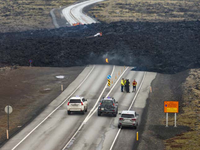 Workers talk in the road in front of a cooling lava flow.