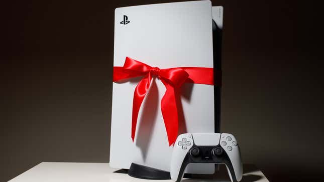 A PlayStation 5 controller is placed on a table in front of a PlayStatoin 5 console that is wrapped in a red bow. PlayStation 5 a