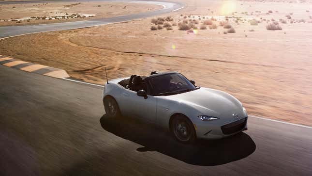 A gray Miata driving on a racetrack with its roof down