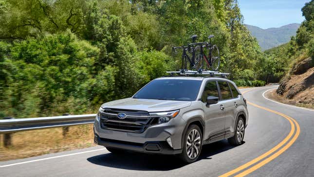 A gray Subaru Forester driving down a mountain road in front of very green trees