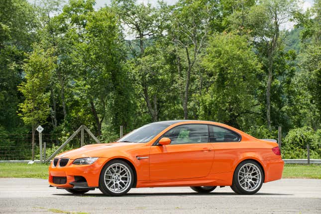 Side view of an orange BMW M3 parked in front of trees.