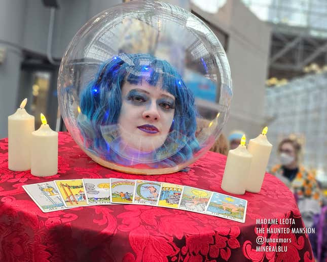 A cosplayer dressed as Madame Leota's head in a crystal ball looks into the camera. A table worn around her neck completes the illusion.