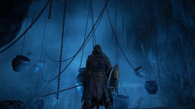 A figure stands in a cave lit with blue-tinted light, with chains behind him, some of them with pots hanging from them.