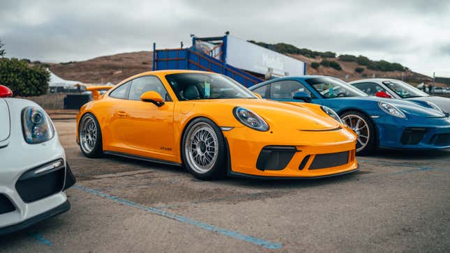 A bright yellow Porsche 911 GT3MR is parked on pavement, it's lowered.