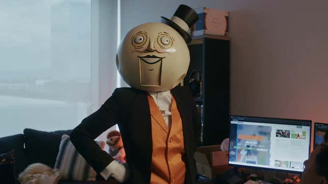 Moon guy with a top hat stands in front of a computer.