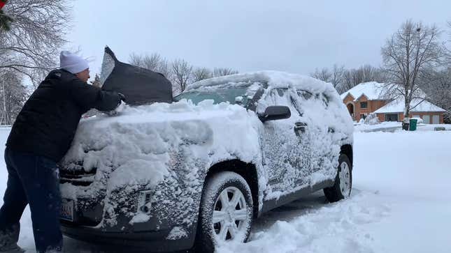 Person removing a windshield snow cover from a crossover, revealing a windshield mostly clear of snow