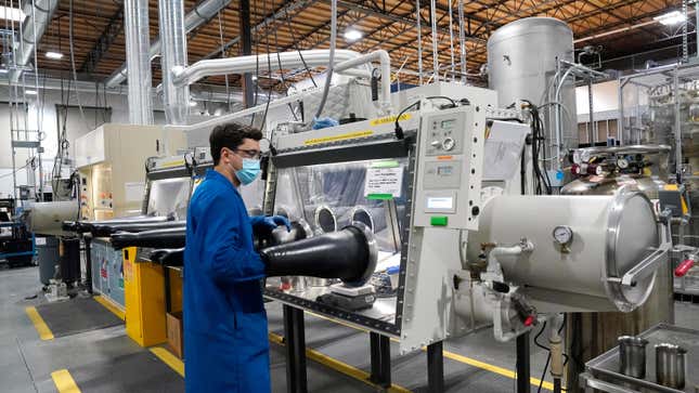 a man wearing a blue safety jacket and a mask in front of a machine, his arms are in two black tubes attached to the machine