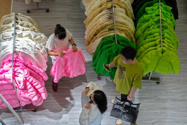 FILE - A woman tries out a fall outfit at a booth doing a promotion sale on clothing for the upcoming autumn season at a shopping mall in Beijing, Sunday, Aug. 20, 2023. China’s economy remains in the doldrums, data released Friday, Oct. 13, showed, with prices falling due to slack demand from consumers and businesses. (AP Photo/Andy Wong, File)