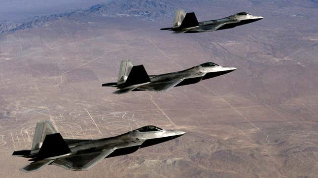 Three F/A-22 Raptor jets flying side-by-side over the Mojave Desert.