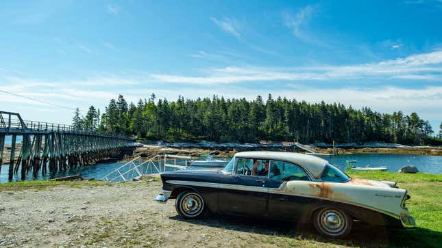 A photo of a vintage car parked by the side of a river in Maine. 