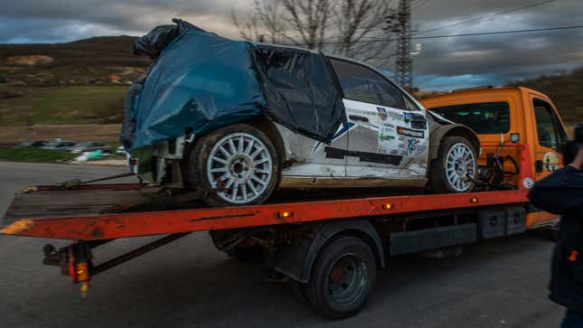 A photo of a crashed rally car on the back of a truck. 
