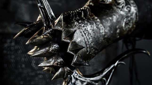 A hand in a spiked, black steel gauntlet grasps the hilt of an ornate sword.