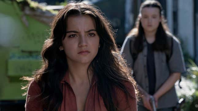 Dina looks at something off-screen while Ellie approaches her from behind.