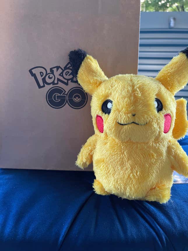 A Pikachu plush is shown next to a paper bag with the Pokemon Go logo on it.