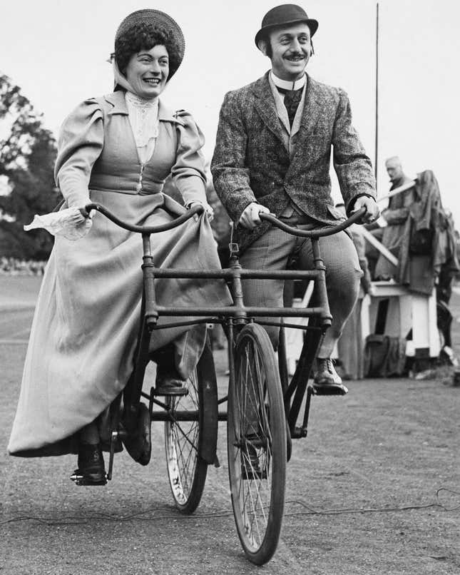 A black and white photo of two people riding a Sociable bike.