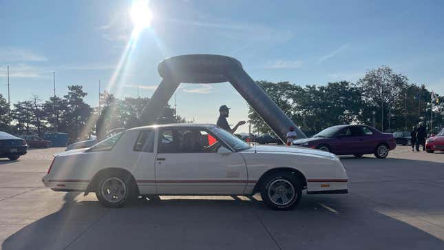 A white car sits in Detroit's Hart Plaza under a metal sculpture on a sunny bright day