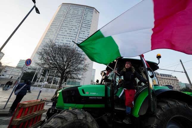 A farmer waves an Italian flag from her tractor in front of the Pirelli skyscraper Lombardy region headquarter, in Milan, Italy, Thursday, Feb. 1, 2024. Farmers have been protesting in various parts of Italy and Europe against EU agriculture policies. (AP Photo/Luca Bruno)