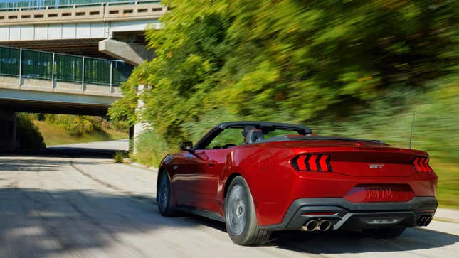 A red Mustang convertible driving with the top down