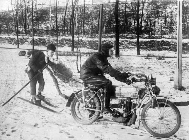 12th January 1912: A motor cyclist pulls a skier along in the snow, in Germany.