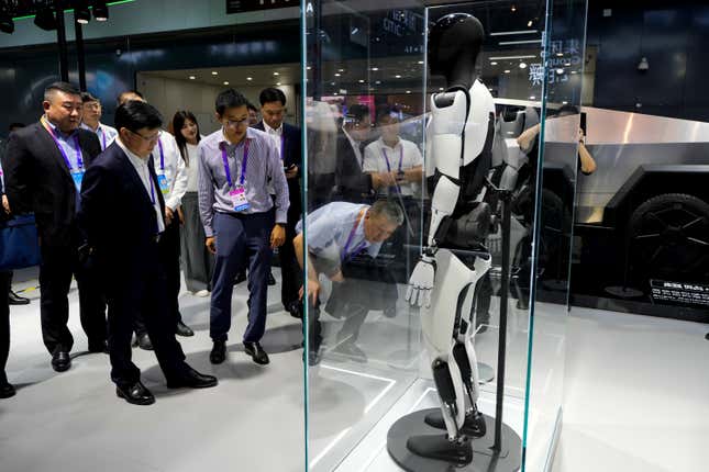 people look at a white Tesla humanoid robot in a glass case