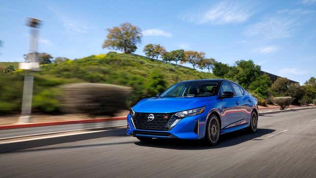 A blue Nissan Sentra driving in front of a grassy knoll