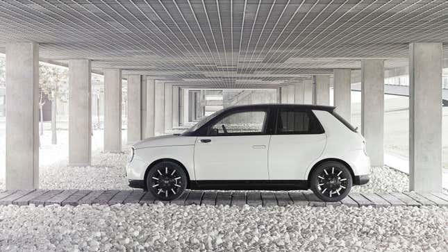 A photo of a white Honda e parked under a bridge. 