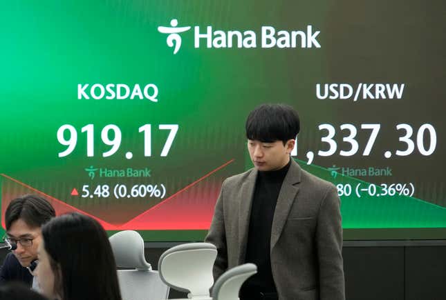 A currency trader passes by the screens showing the Korea Composite Stock Price Index (KOSPI), left, and the foreign exchange rate between U.S. dollar and South Korean won at the foreign exchange dealing room of the KEB Hana Bank headquarters in Seoul, South Korea, Tuesday, March 26, 2024. Asian shares were mixed in muted trading Tuesday, as buying in some markets was soon erased by profit-taking. (AP Photo/Ahn Young-joon)