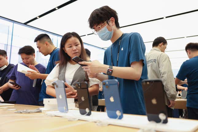 a man in a navy Apple t-shirt shows a woman an iPhone in front of a display of iPhones