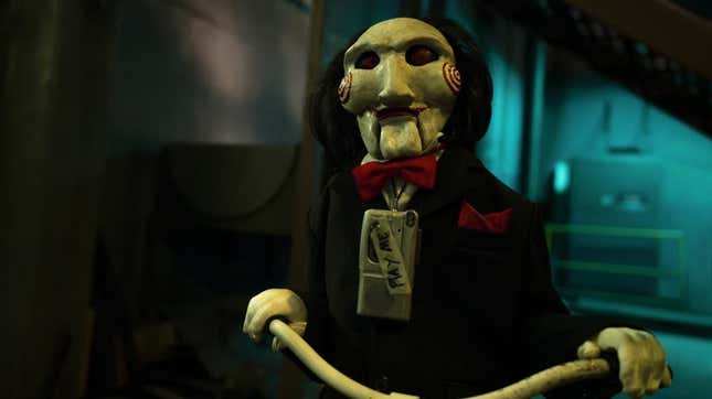 Billy the puppet sits on a tricycle with a tape recorder around his neck that says "PLAY ME."