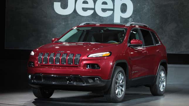 Une Jeep Cherokee rouge garée devant un grand panneau Jeep 