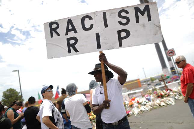 A man carries a ‘Racism RIP’ sign at a makeshift memorial honoring victims outside Walmart, near the scene of a mass shooting which left at least 22 people dead, on Aug. 6, 2019, in El Paso, Texas. A 21-year-old white male suspect remains in custody.