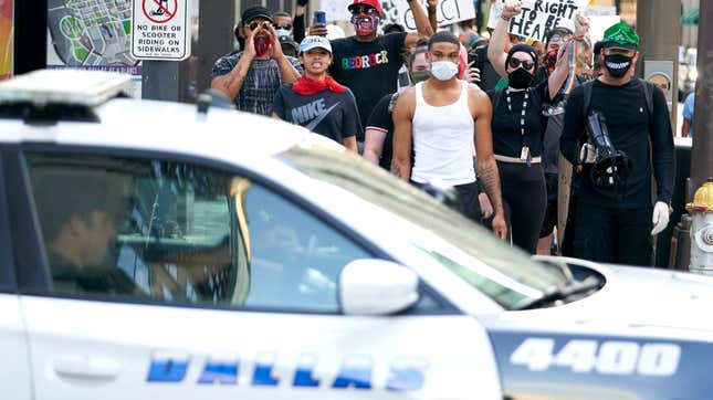 DALLAS, TX - JUNE 06: Demonstrators march past a Dallas Police car during a peaceful protest against police brutality and racism on June 6, 2020 in Dallas, Texas. This is the 12th day of protests since George Floyd died in Minneapolis police custody on May 25. 