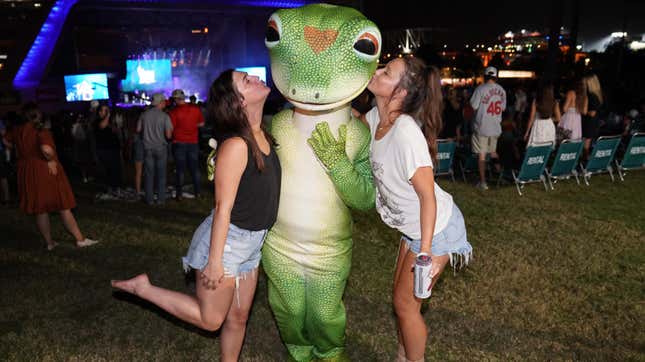 two women kissing a person dressed as the Geico gecko at a concert