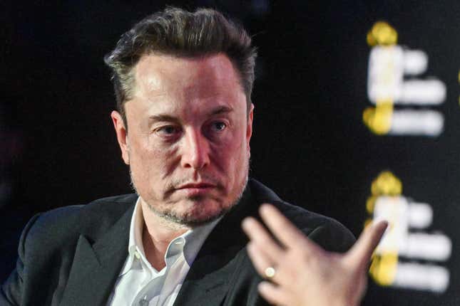 A close-up of Elon Musk as he looks of frame toward someone who is talking to him