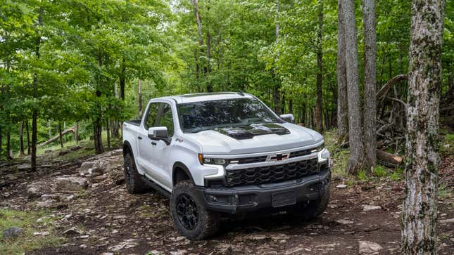 A photo of a white Chevrolet Silverado pickup in a forrest. 