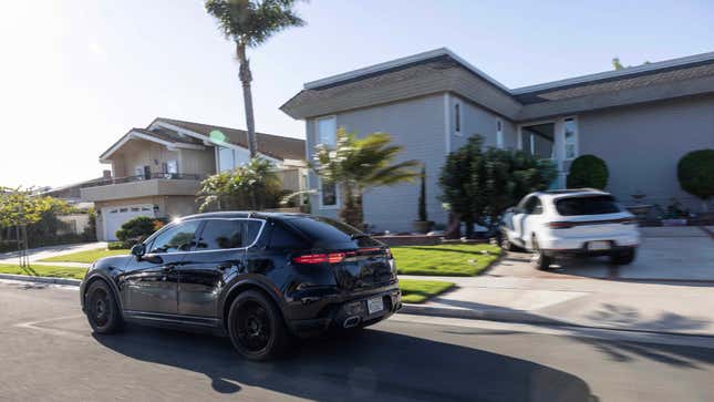Rear 3/4 view of a camouflaged black Porsche Macan EV driving down a residential street