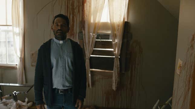 A priest stands in front of a wall covered in blood.