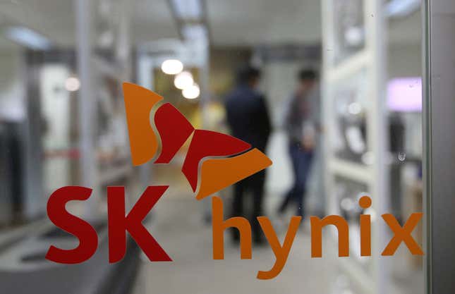 red and orange logo of SK Hynix on glass door, there are blurry figures of people walking behind the door