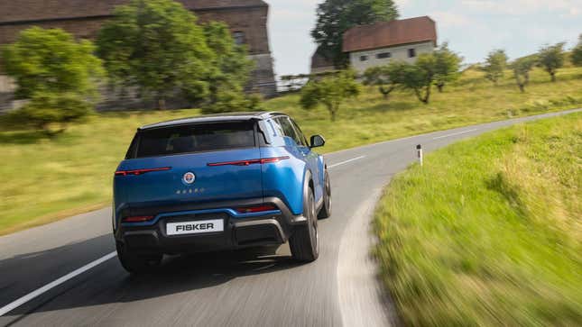 the rear of a blue Fisker Ocean driving around a bend on a rural road