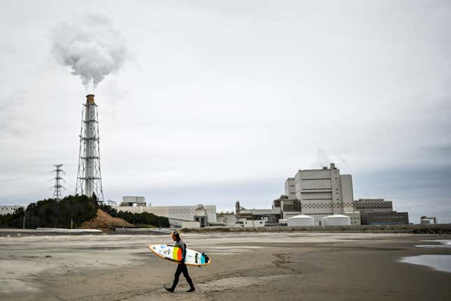 Koji Suzuki, a surfer and a surf shop owner, walking on the beach in front of a thermal power station after a surfing session in Minamisoma, Fukushima prefecture.
