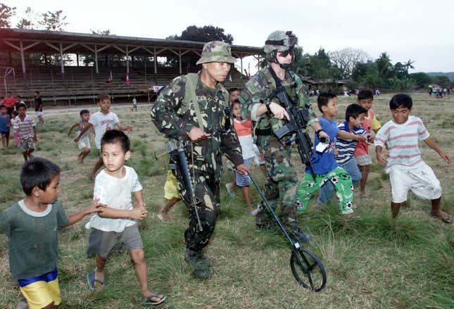 A Filipino soldier and American Green Beret are joined by local children asthey survey an athletic field for possible use as a landing area in 2002.