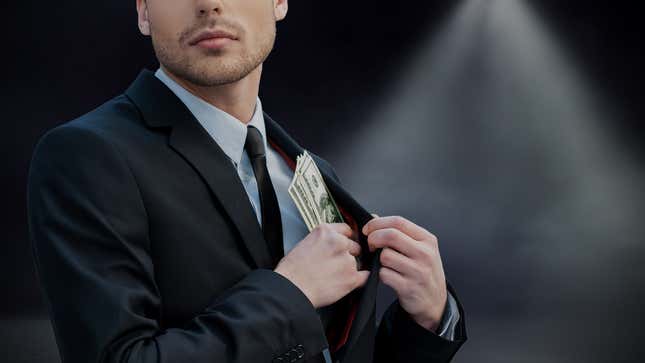 An anonymous stock-image businessman looks around as he tucks U.S. dollars into his lapel pocket.