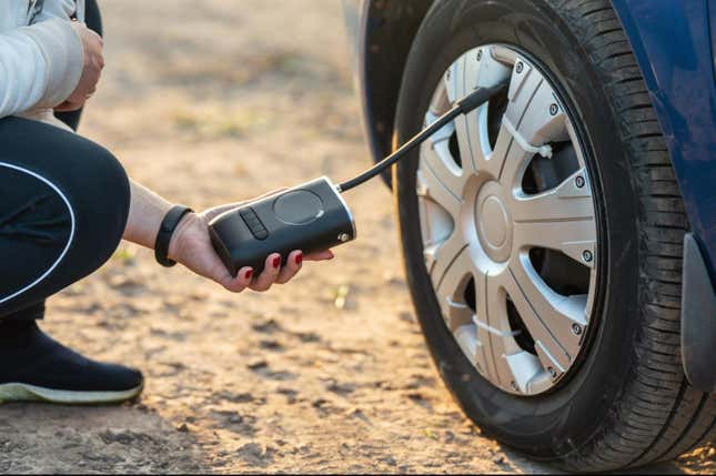 A close up of a person using a portable air compressor to inflate a tire with a hubcap held on by zipties