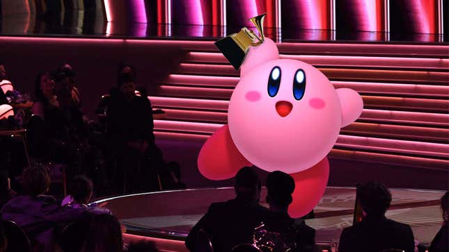 Kirby holds up a Grammy triumphantly while standing adorably on the award stage. 