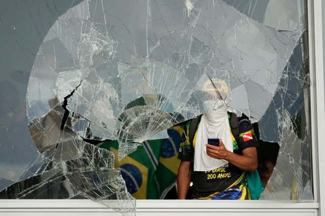 FILE - Supporters of Brazil&#39;s former President Jair Bolsonaro, look out from a shattered window after they stormed the Planalto presidential palace in Brasilia, Brazil, Jan. 8, 2023. A year later, around 400 people remain jailed facing charges for the riots and Bolsonaro has been under investigation by the Supreme Court about his role in the mayhem. (AP Photo/Eraldo Peres, File)