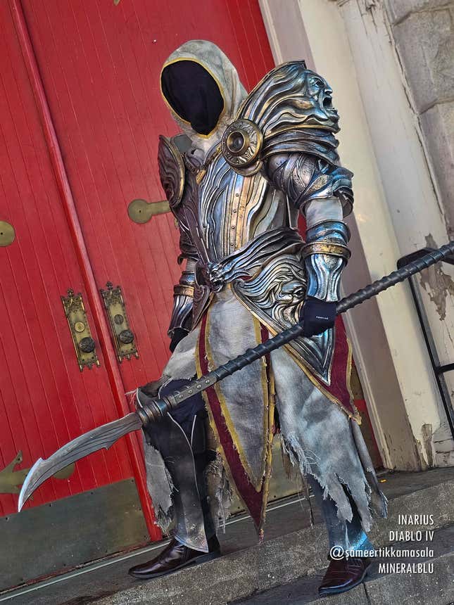 A cosplayer stands in front of a red door dressed as Inarius from Diablo IV. 