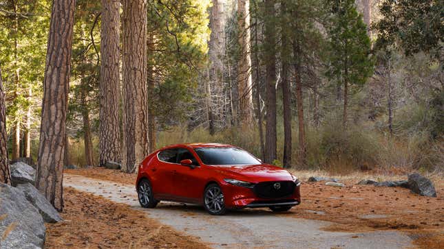 A red Mazda 3 sedan in a forrest 